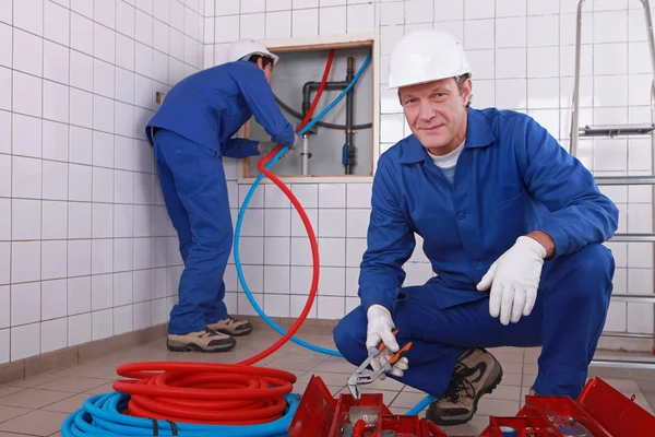 Dos fontaneros trabajando, un fontanero está conectando tuberías —  Fotos de Stock