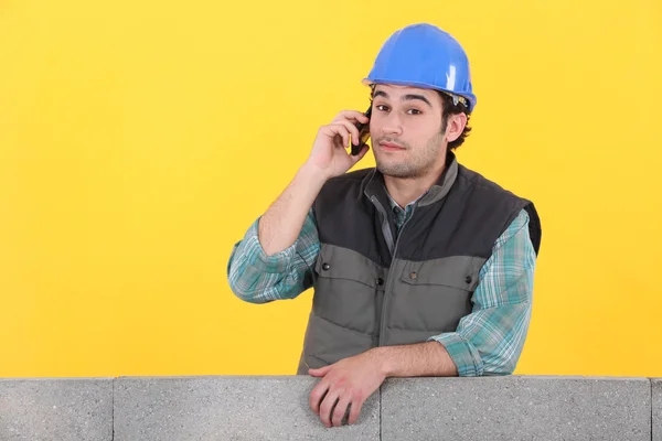 노란색 backgroun에 대 한 콘크리트 벽 뒤에 전화에 젊은 벽돌공 — 스톡 사진