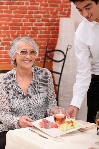 Young waiter serving an older woman in a restaurant — Stock Photo, Image