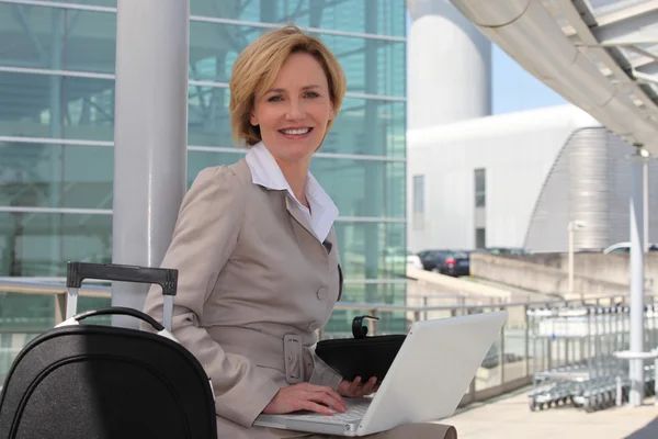Geschäftsfrau lächelt auf Laptop vor Flughafen — Stockfoto