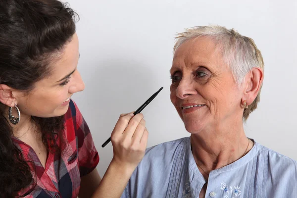 Jovem mulher aplicando maquiagem para uma senhora idosa — Fotografia de Stock