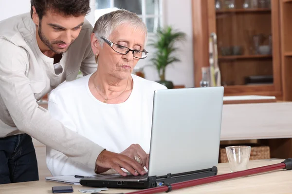 Jovem ajudando um idoso com um computador portátil — Fotografia de Stock