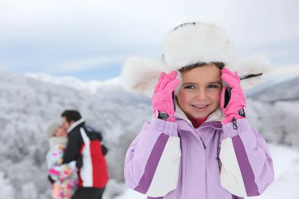 Liten flicka i snön i närheten av föräldrar — Stockfoto