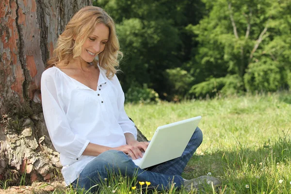 Mulher loira sentou-se à árvore com computador portátil — Fotografia de Stock