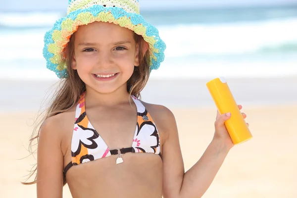 Young girl on the beach holding suncream — Stock Photo, Image