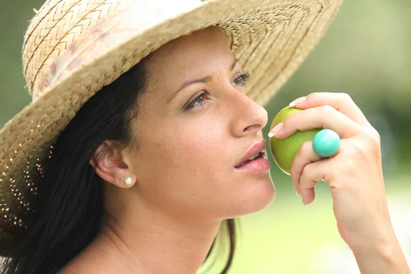 Женщина в соломенной шляпе собирается укусить яблоко — стоковое фото