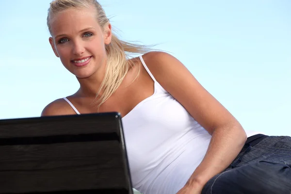 Genç kadın mavi gökyüzü karşı bir dizüstü bilgisayar kullanarak — Stok fotoğraf