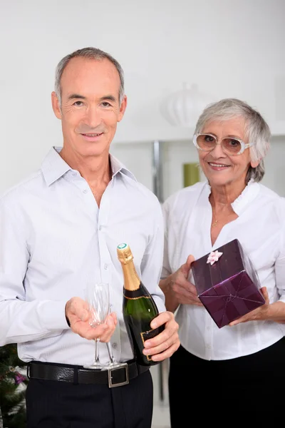 Старшая пара с шампанским и подарком — стоковое фото
