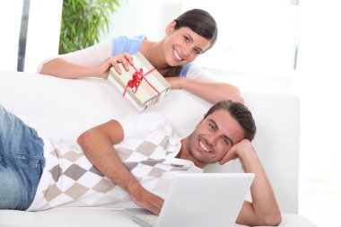 Woman handing gift to man on sofa clipart