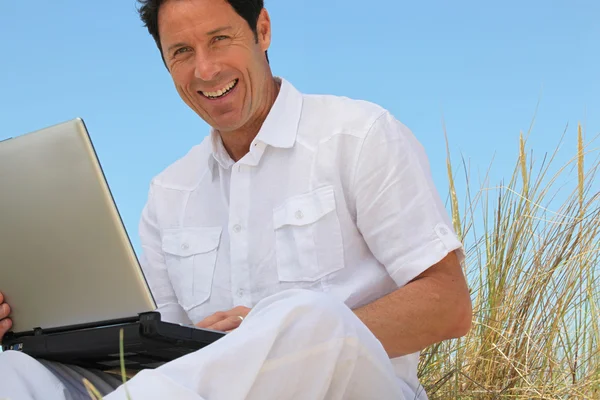 Man smiling on laptop in blue sky — Stock Photo, Image