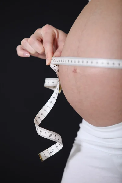 Mujer embarazada sosteniendo una cinta métrica alrededor de su bulto —  Fotos de Stock