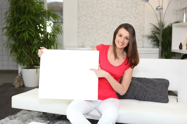 stock image Woman sitting on a sofa with a board left blank for your message