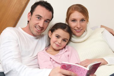 Parents reading a bedtime story to their daughter clipart