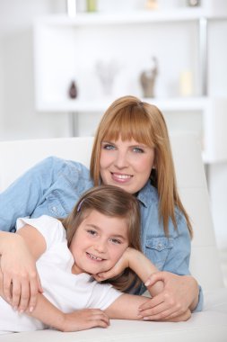 A 35 years old mother and her little girl lying down on a couch clipart