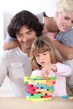 Parents looking her daughter playing with blocks clipart