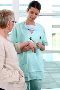 A nurse testing reflexes of a patient clipart