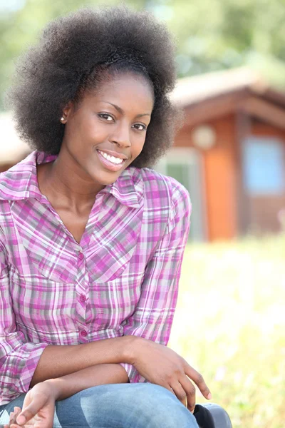 Woman in pink checked shirt sitting in front of wooden cabin — Stock Photo, Image