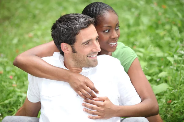 Para mieszanej rasy przytulanie na trawie — Zdjęcie stockowe