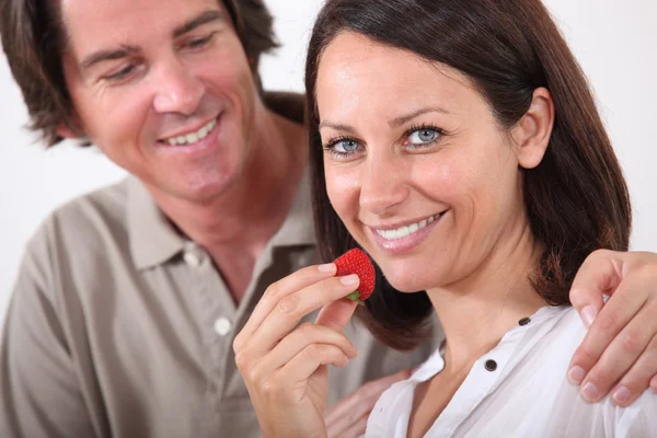 Mann umarmt seine Frau, während sie Erdbeeren isst — Stockfoto