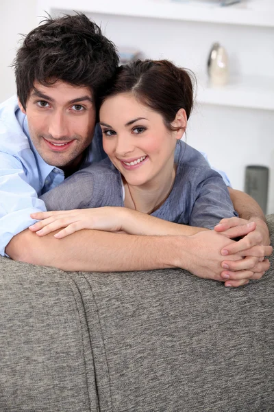 Para przytulanie za kanapą — Zdjęcie stockowe