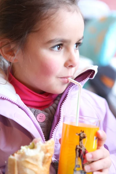 Девочка пьет апельсиновый сок через соломинку — стоковое фото