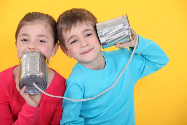 Barnen att ha ett telefonsamtal med konservburkar på gul bakgrund — Stockfoto