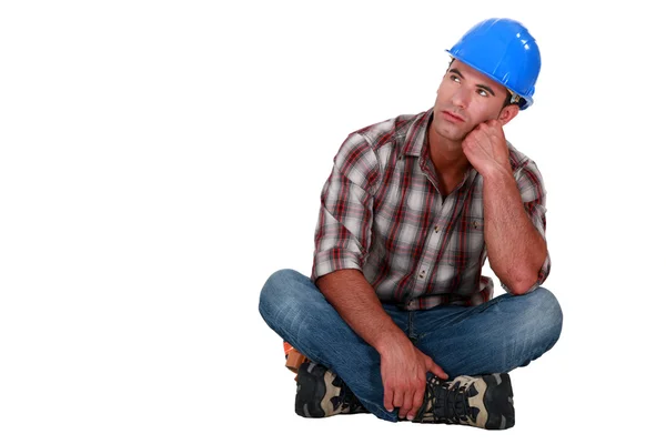 En fundersam byggnadsarbetare som sitter på golvet. — Stockfoto