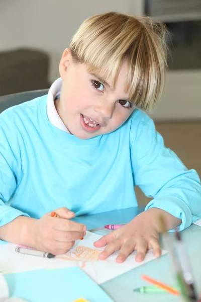 Маленький мальчик рисует в школе восковыми карандашами — стоковое фото