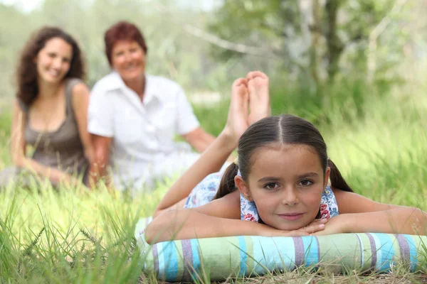Niña relajándose en el parque con la madre y la abuela en el fondo —  Fotos de Stock