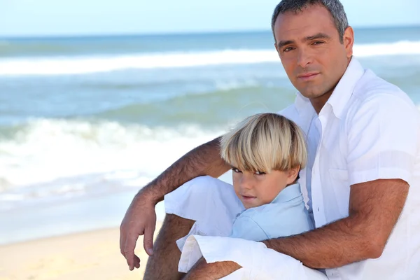 Otec a syn sedí na pláži — Stock fotografie