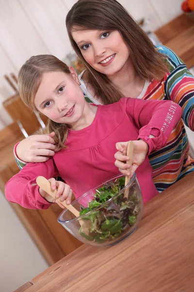 Mujer joven y niña pequeña mezclando una ensalada verde en un tazón — Foto de Stock