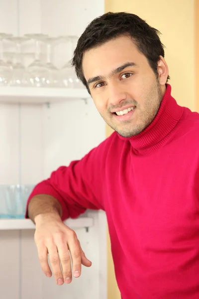 Young man standing next to a cupboard full of glasses — Stock Photo, Image