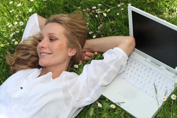 Гарненька леді розкладається в траві поруч з ноутбуком комп'ютера — стокове фото