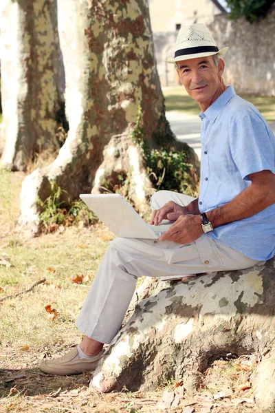 Bir ağaç kütüğü üzerinde oturan ve onun dizüstü bilgisayarda çalışan adam — Stok fotoğraf