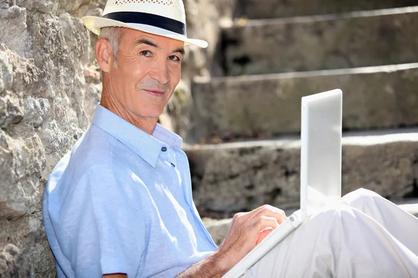 Homem aposentado sentou-se contra a parede de pedra com laptop — Fotografia de Stock