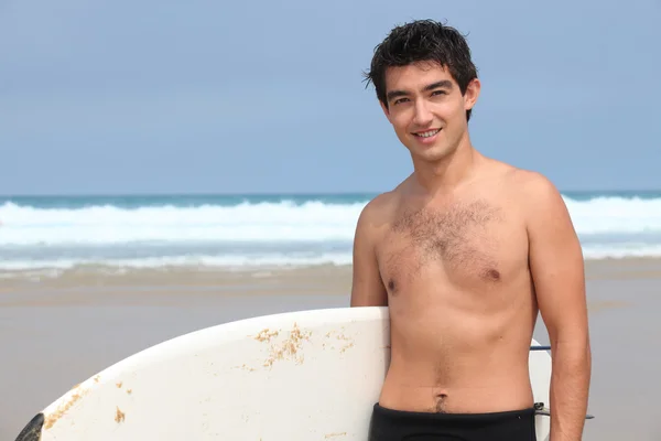 Молодой человек на пляже с доской для серфинга — стоковое фото