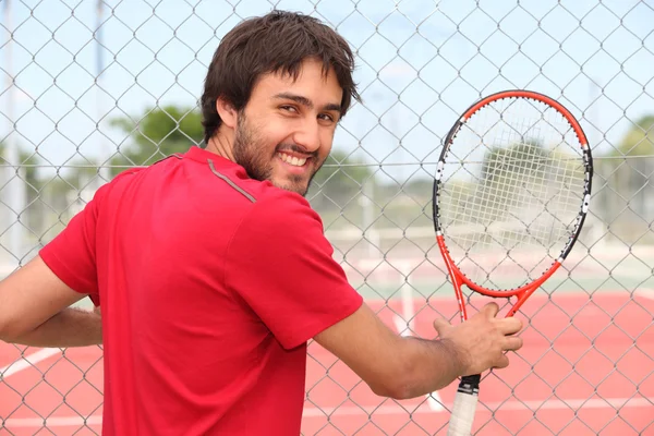 Hombre sonriente sosteniendo raqueta por valla de pista de tenis municipal —  Fotos de Stock