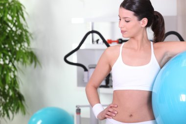 Woman standing with an exercise ball at the gym clipart