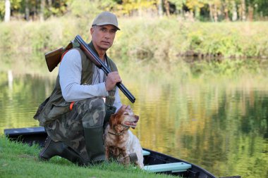 A hunter and his dog by a river. clipart