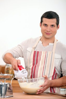 Young man using an electric egg beater clipart