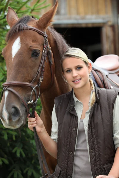 Junge blonde Frau und ein Pferd vor einem Stall — Stockfoto