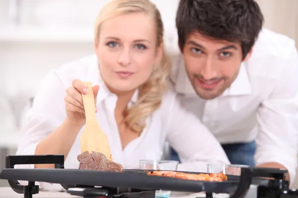 Una pareja frente a la cámara y mostrando carne cocida sobre una plancha eléctrica c — Foto de Stock