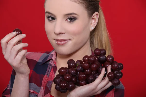 Junge Frau isst Weintrauben auf rotem Hintergrund — Stockfoto