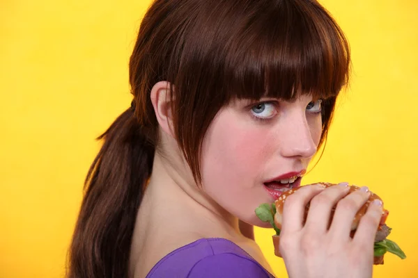 Fiatal barna hajú nő, eszik egy hamburgert — Stock Fotó