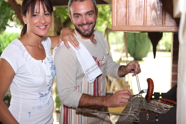 Couple cuisiner des saucisses sur le barbecue — Photo