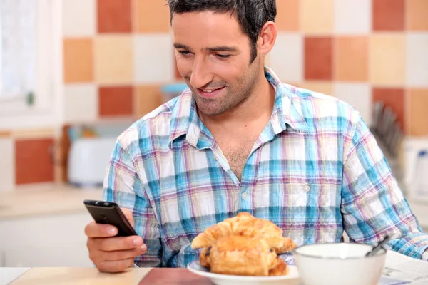 Man eating croissant and texting — Stock Photo, Image