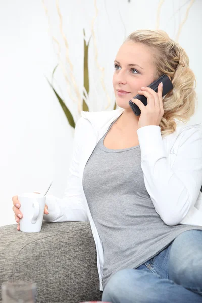 Žena uvolňující na pohovce s kávou a telefon — Stock fotografie
