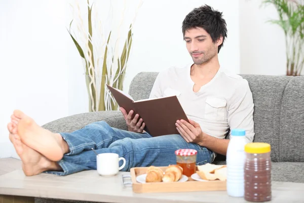 Человек расслабился на диване с альбомом во время завтрака — стоковое фото