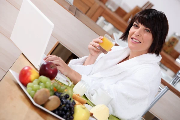 Mulher usando um laptop enquanto come um café da manhã frutado — Fotografia de Stock