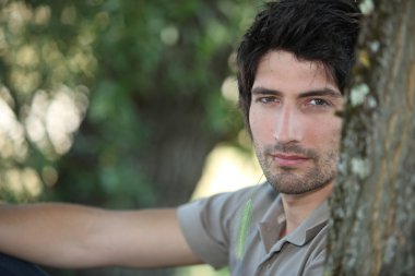 Closeup of a handsome young man sitting amongst the trees clipart